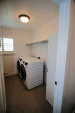 Laundry area with washing machine and dryer, dark tile patterned flooring, laundry area, and baseboards