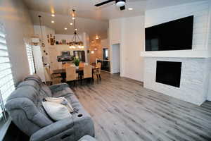 Living room with a stone fireplace, recessed lighting, light wood-type flooring, and ceiling fan with notable chandelier