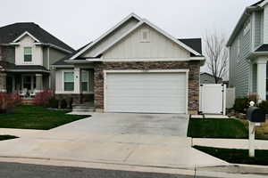 View of front of home featuring concrete driveway, an attached garage, stone siding, board and batten siding, and a gate