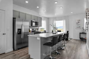 Kitchen with stainless steel appliances, gray cabinetry, a breakfast bar, a center island with sink, and wood finished floors