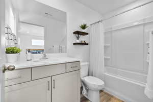 Full bath featuring visible vents, toilet, wood finished floors, vanity, and shower / tub combo