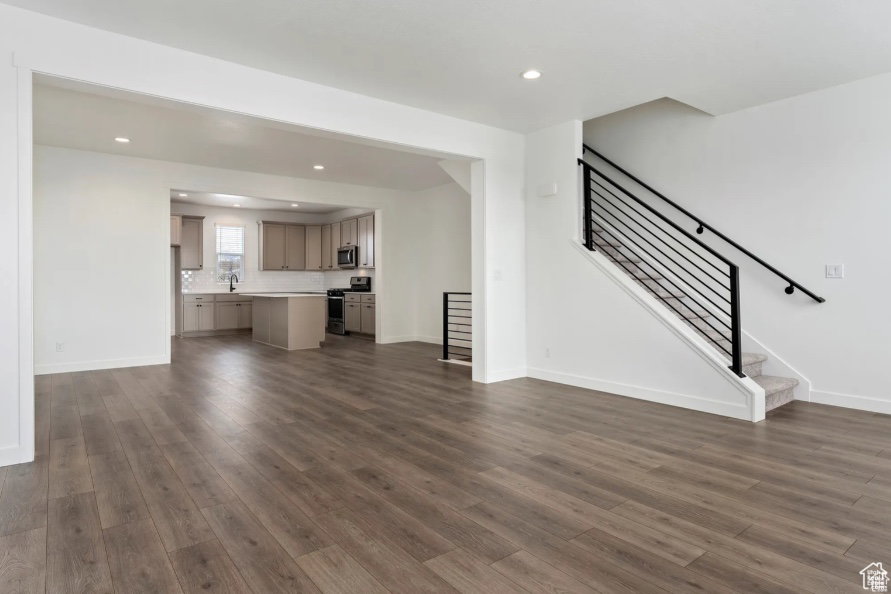 Unfurnished living room featuring dark wood-style floors, baseboards, stairs, and recessed lighting