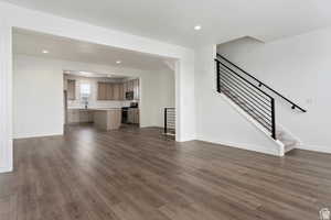 Unfurnished living room featuring dark wood-style floors, baseboards, stairs, and recessed lighting