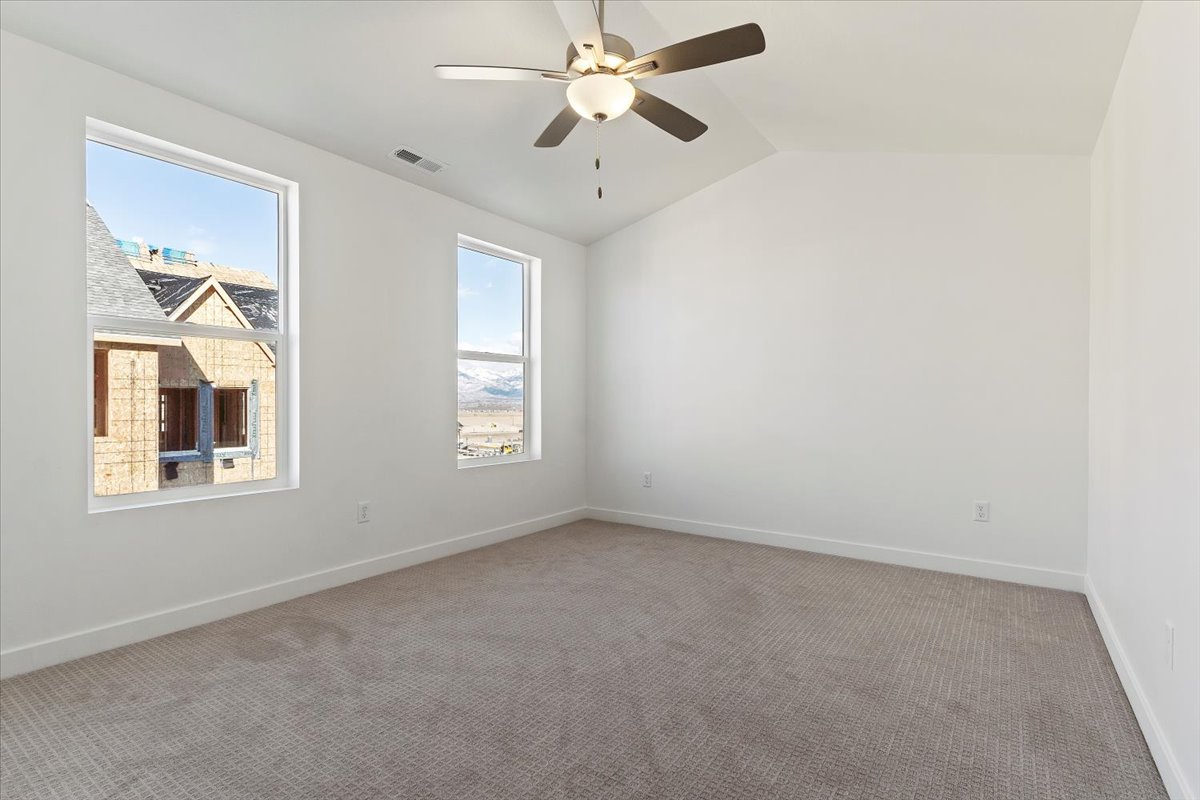 Unfurnished room featuring visible vents, baseboards, a ceiling fan, light carpet, and lofted ceiling