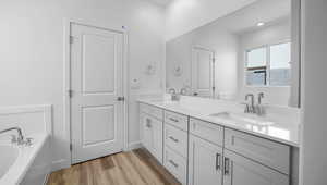Full bathroom featuring double vanity, a sink, a garden tub, and wood finished floors