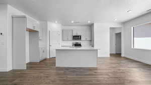 Kitchen with an island with sink, light countertops, stainless steel appliances, visible vents, and dark wood-style flooring