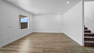 Empty room featuring baseboards, stairs, wood finished floors, and recessed lighting