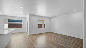 Unfurnished living room featuring recessed lighting, a textured ceiling, baseboards, and wood finished floors
