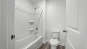 Bathroom featuring baseboards, shower / tub combination, wood finished floors, and toilet