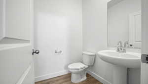 Half bath featuring baseboards, toilet, and wood finished floors