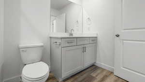 Bathroom featuring toilet, vanity, baseboards, and wood finished floors