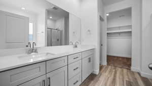 Bathroom featuring visible vents, a shower stall, double vanity, wood finished floors, and a sink