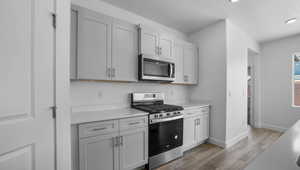 Kitchen with light countertops, wood finished floors, a textured ceiling, stainless steel appliances, and baseboards