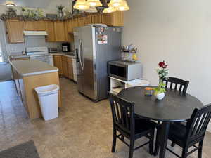 Kitchen featuring light countertops, pendant lighting, a kitchen island, appliances and under cabinet range hood