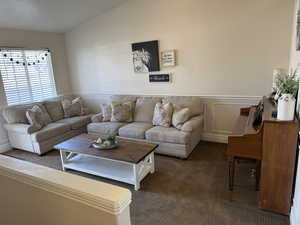 Living room with carpet floors, a decorative wall, and wainscoting