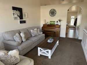 Living area featuring a decorative wall, a wainscoted wall, arched walkways, and neutral carpet
