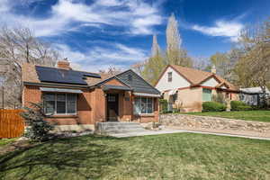 Bungalow-style home with brick siding, a front lawn, and roof mounted solar panels
