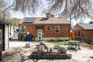 Back of house featuring roof with shingles, a patio area, brick siding, fence, and roof mounted solar panels