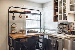 Interior space featuring glass insert cabinets, open shelves, dishwasher, butcher block countertops, and decorative backsplash