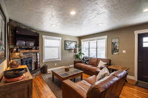 Living area featuring a textured ceiling, baseboards, a stone fireplace, and hardwood / wood-style flooring