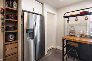 Kitchen featuring butcher block countertops, white cabinetry, baseboards, and stainless steel fridge
