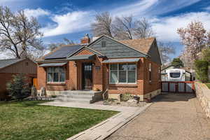 Bungalow-style home with solar panels, a chimney, brick siding, a front lawn, and roof with shingles
