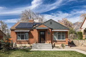 Bungalow-style home with brick siding, a chimney, and roof mounted solar panels