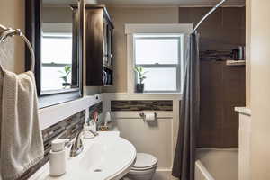 Bathroom with a sink, backsplash, toilet, and shower / bath combo