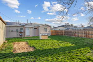 Rear view of property featuring a fenced backyard, solar panels, and a lawn