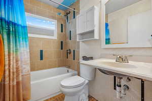Full bathroom featuring tile walls, decorative backsplash, toilet, and shower / tub combo