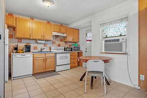 Kitchen with light countertops, white appliances, under cabinet range hood, a sink, and light tile patterned flooring