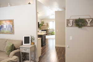Living room with dark wood-type flooring, a fireplace, baseboards, and vaulted ceiling
