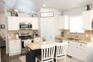 Kitchen with white cabinetry, a sink, appliances with stainless steel finishes, and lofted ceiling