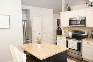 Kitchen with white cabinetry, decorative backsplash, a kitchen island, light stone countertops, and appliances with stainless steel finishes