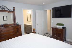 Bedroom featuring ensuite bathroom, baseboards, and light colored carpet
