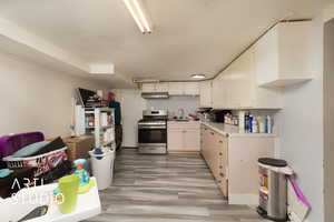 Kitchen with light countertops, a sink, light wood finished floors, under cabinet range hood, and gas stove