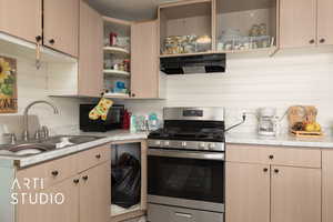 Kitchen with stainless steel range with gas stovetop, under cabinet range hood, backsplash, and light brown cabinetry