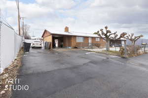 View of front of house with aphalt driveway, a chimney, fence, and a carport