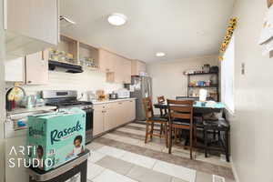 Kitchen featuring light countertops, a sink, open shelves, under cabinet range hood, and stainless steel appliances