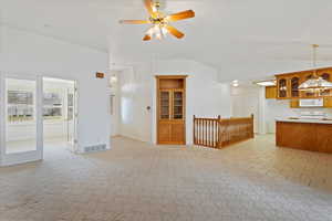 Interior space with light carpet, ceiling fan with notable chandelier, lofted ceiling, and visible vents