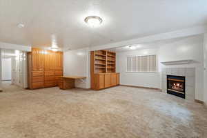Interior space featuring light carpet, baseboards, a tiled fireplace, and a textured ceiling