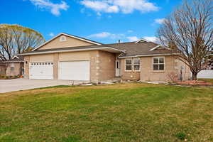 Ranch-style home featuring an attached garage, brick siding, a front lawn, and driveway