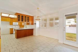Kitchen with light countertops, white appliances, a peninsula, brown cabinetry, and glass insert cabinets