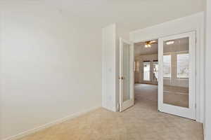 Empty room featuring french doors, baseboards, light colored carpet, and ceiling fan