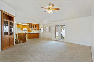 Unfurnished living room featuring lofted ceiling, baseboards, visible vents, light carpet, and ceiling fan