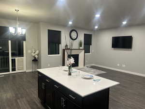 Kitchen with dark cabinets, dark wood-type flooring, light countertops, baseboards, and a notable chandelier