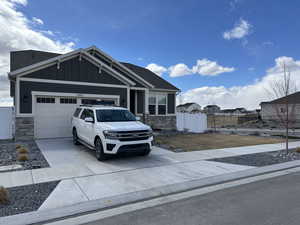Craftsman house featuring board and batten siding, fence, stone siding, an attached garage, and driveway