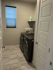 Clothes washing area with washer and clothes dryer, light wood finished floors, laundry area, and baseboards