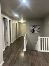 Hallway featuring baseboards, an upstairs landing, and dark wood finished floors, Stairway to fully finished walkout basement