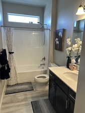 Full bathroom with toilet, a wealth of natural light, shower / bath combo with shower curtain, and wood finished floors